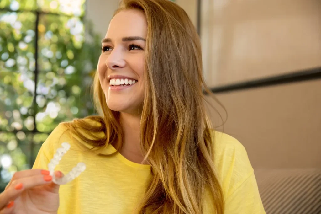 En leende kvinna i gul tröja håller i aligners för tandreglering